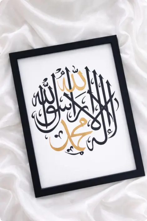 Elegant Islamic calligraphy wall frame with black and gold Arabic lettering placed on a soft white fabric background, perfect for home décor and customized Gifts Hampers in Thrissur.