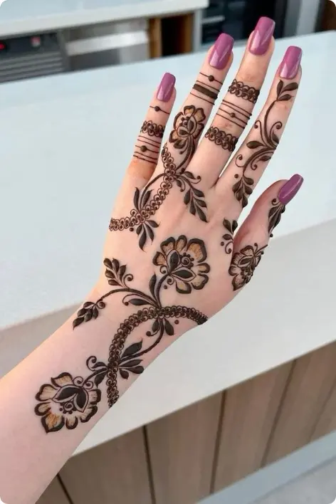 Elegant floral mehndi design on a woman’s hand featuring detailed Arabic-style patterns, leafy vines, and flower motifs with glossy pink nails, showcasing creative henna artistry and customized Gifts Hampers in Thrissur.
